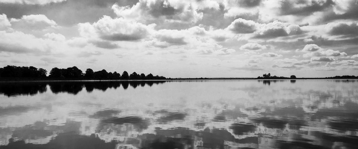 Clouds reflected in the still surface of Craigmaddie Reservoir, in black and white