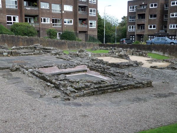 The stone foundations of the Roman bath house in Bearsden, with flats behind